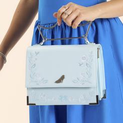 Elegancia de cuento con un guiño moderno. El Bolso bandolera Cenicienta de Disney Loungefly luce un azul hielo con destellos finos, bordados florales en relieve y un aplique metálico del mítico zapatito